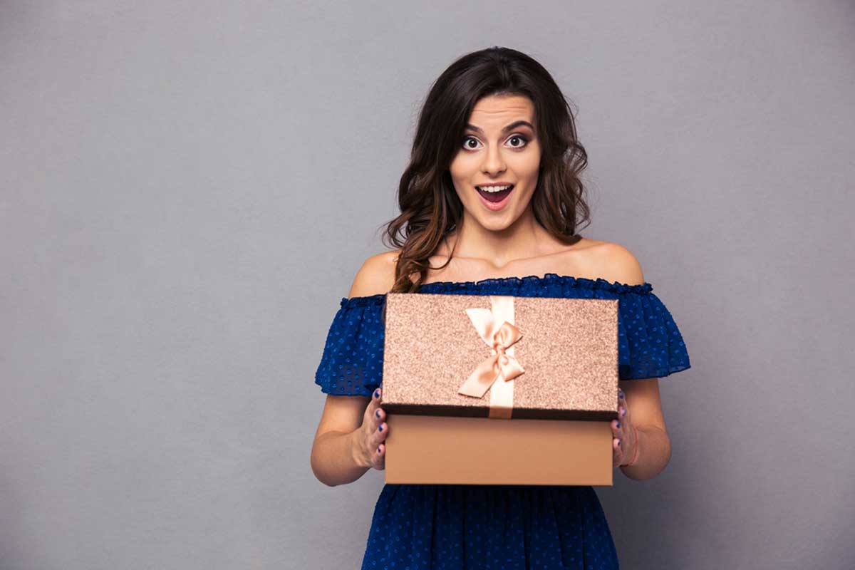 Portrait of a happy woman opening gift box and looking at camera over gray background